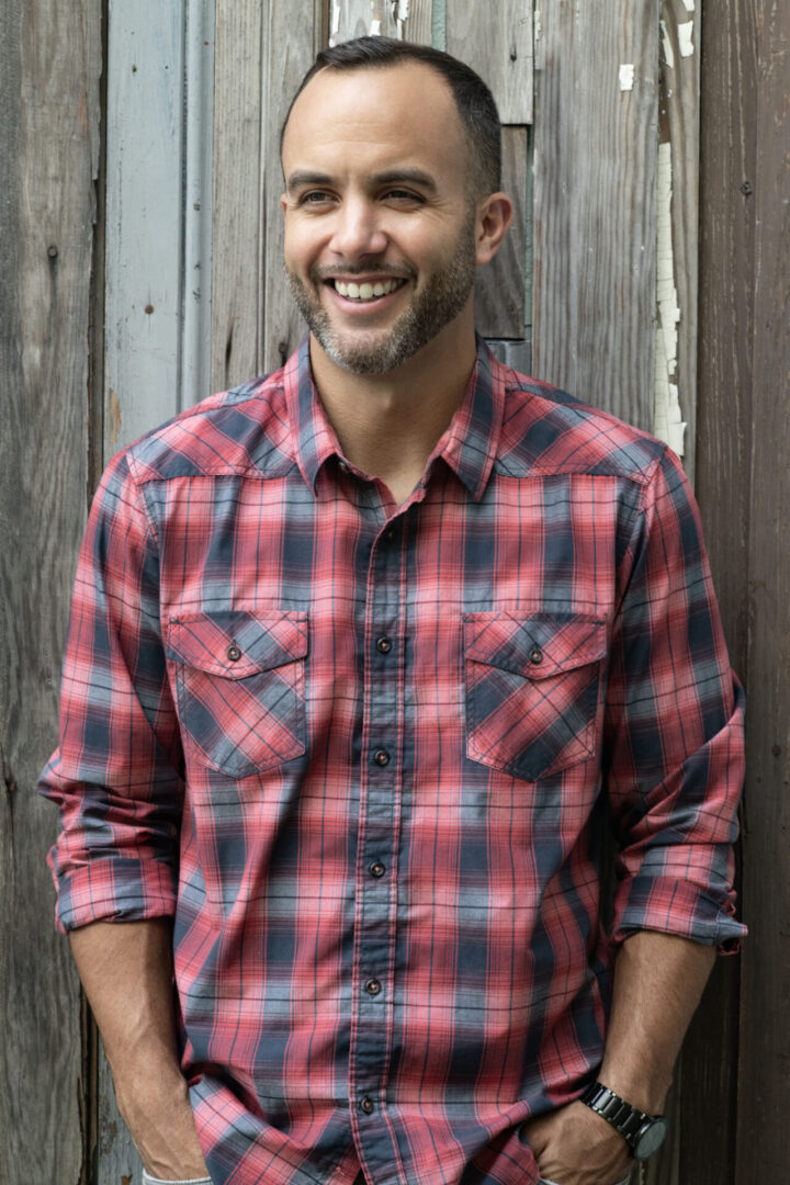 A man in a red and blue plaid shirt smiling.