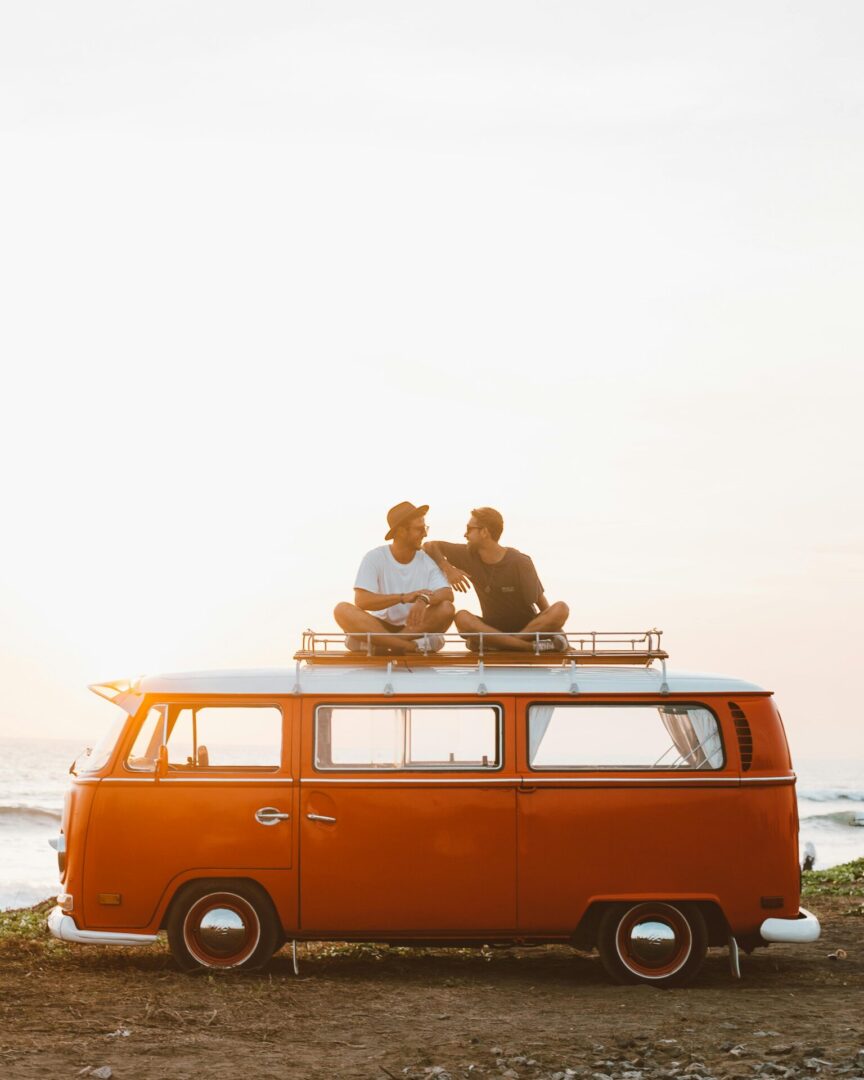 Two men sitting on top of a red van.